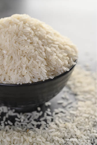 Milled rice in a black bowl on the black cement floor. Selective focus