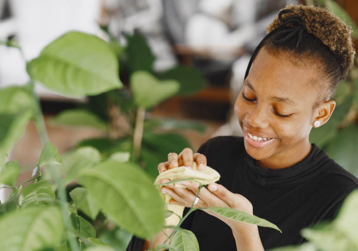 Woman at home. Girl in a black sweater. African woman use the rag. Person with flowerpot.