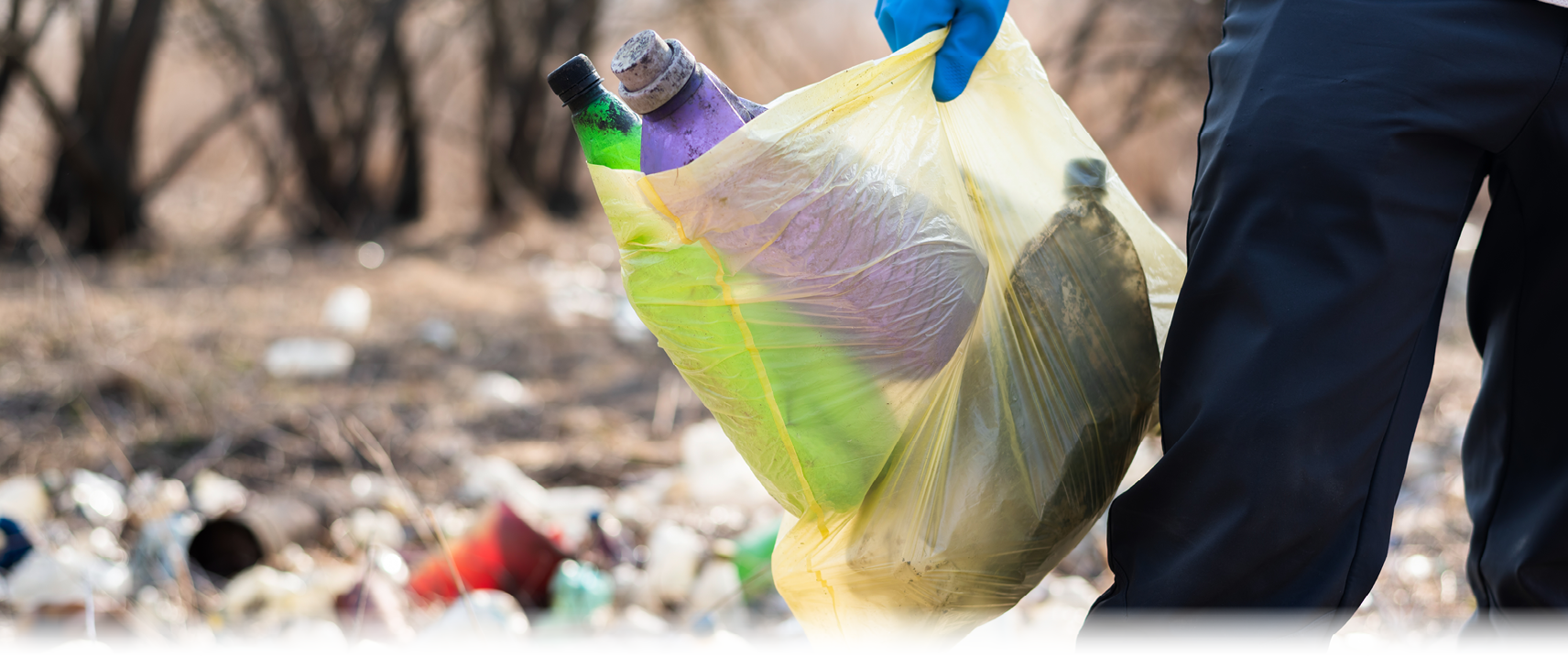 Man in gloves collecting scattered plastic bottles from the ground in the nature