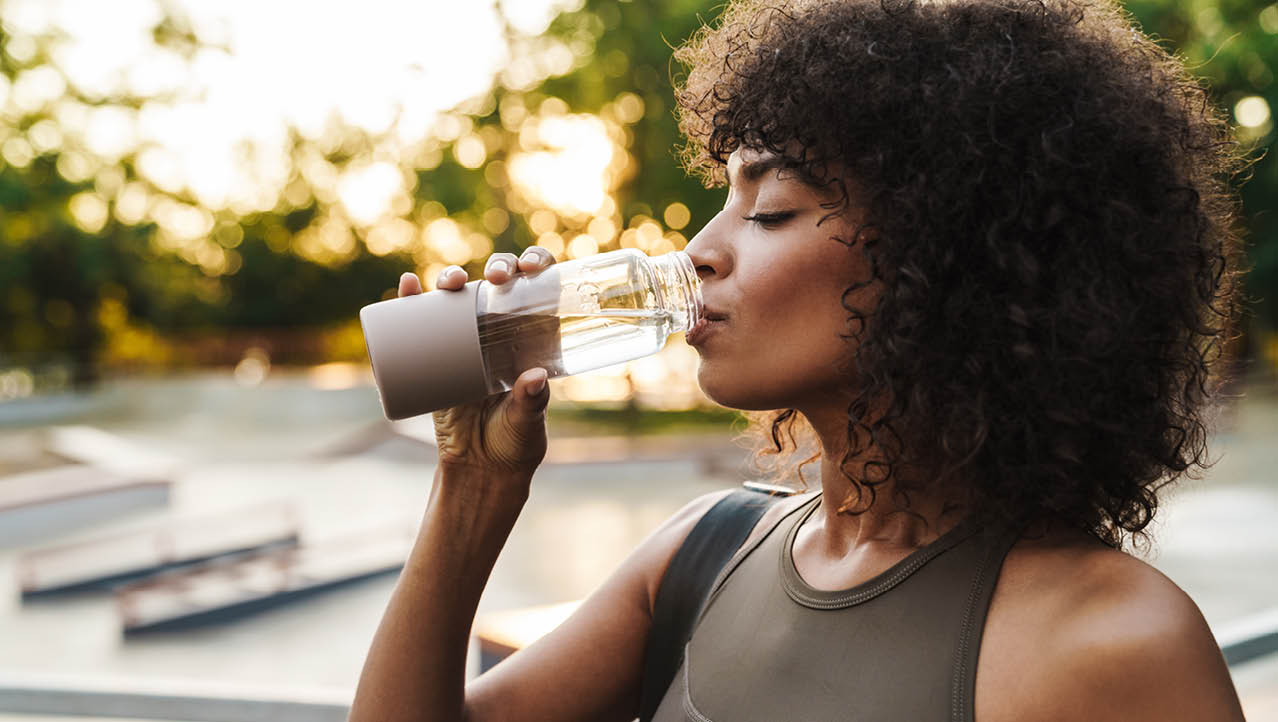 Image of african american sportswoman drinking water while working out on sports ground