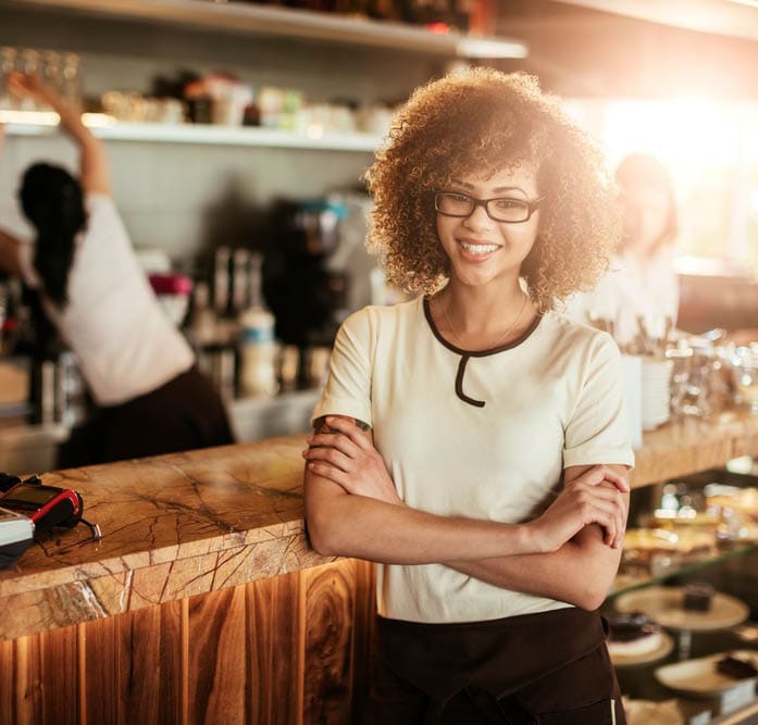 Portrait of a young female barista looking at the camera with crossed arms in a cafe