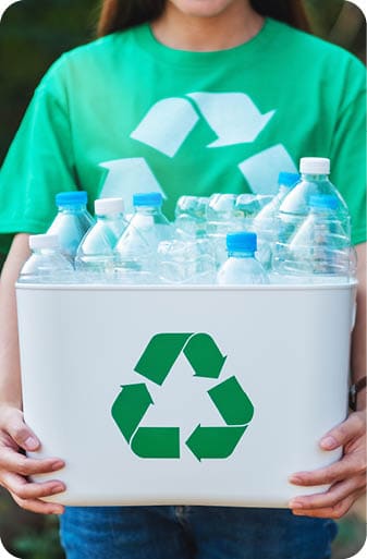 A woman collecting garbage and holding a recycle bin with plastic bottles in the outdoors