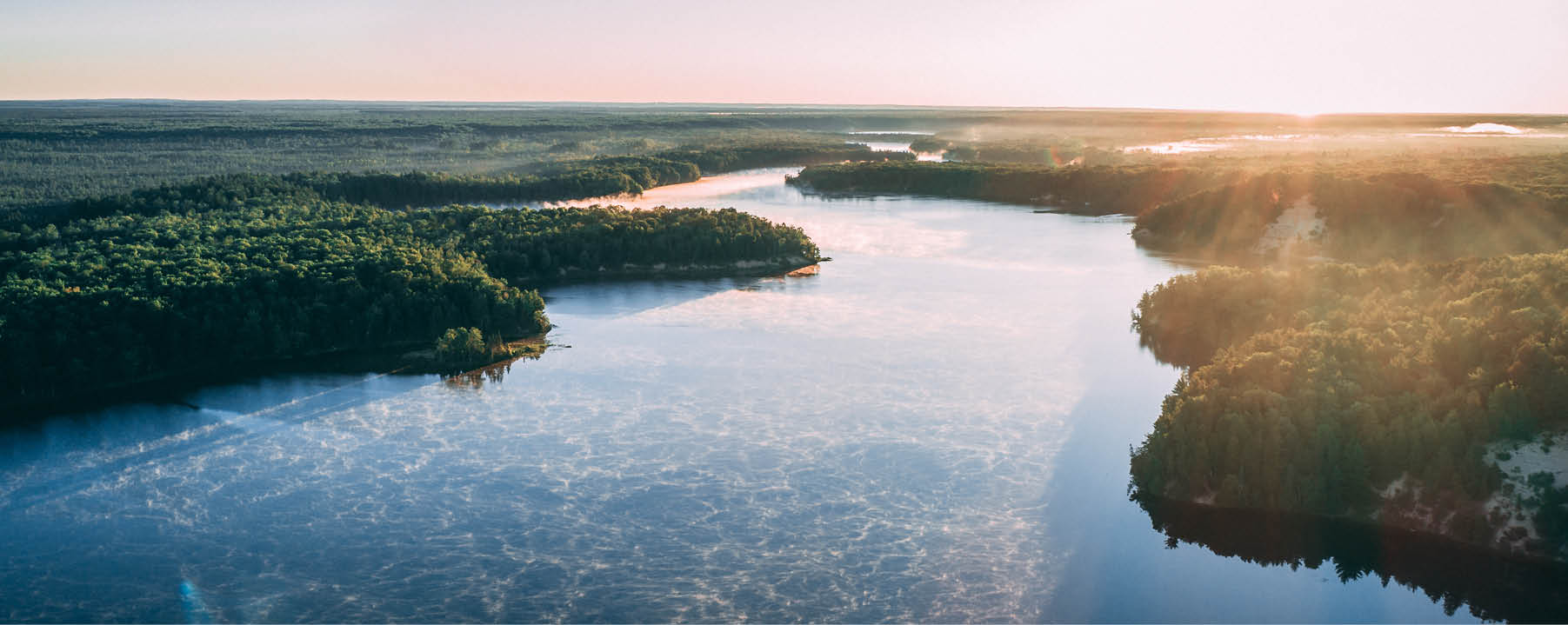 An aerial picture of a river surrounded by islands covered in greenery under sunlight